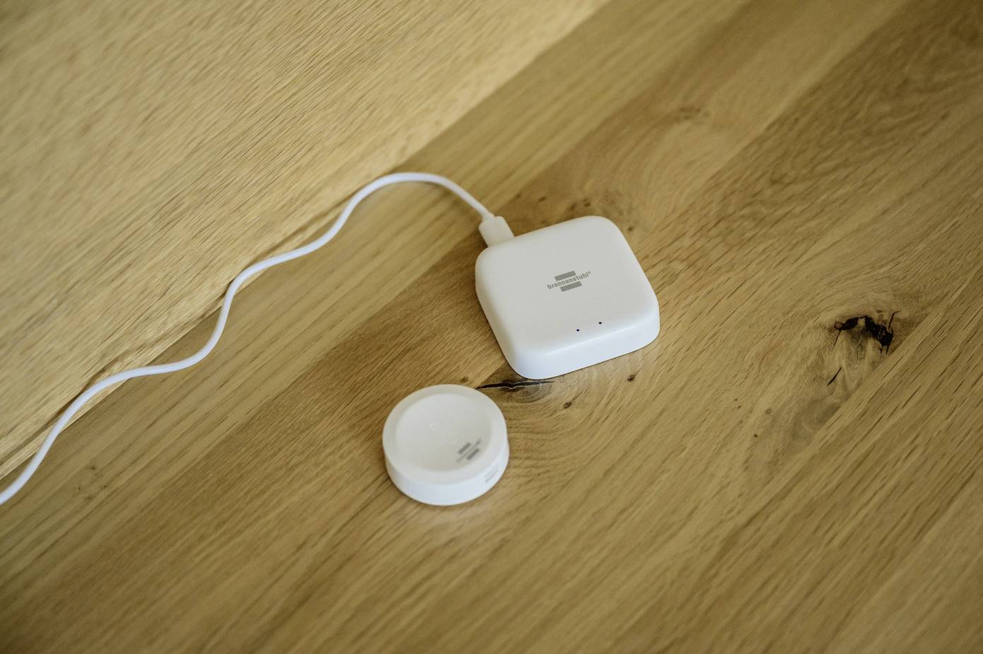 Bílé elektronické zařízení a senzor s kabelem na dřevěném povrchu. Zařízení pro monitorování nebo ovládání v inteligentním domácím systému.