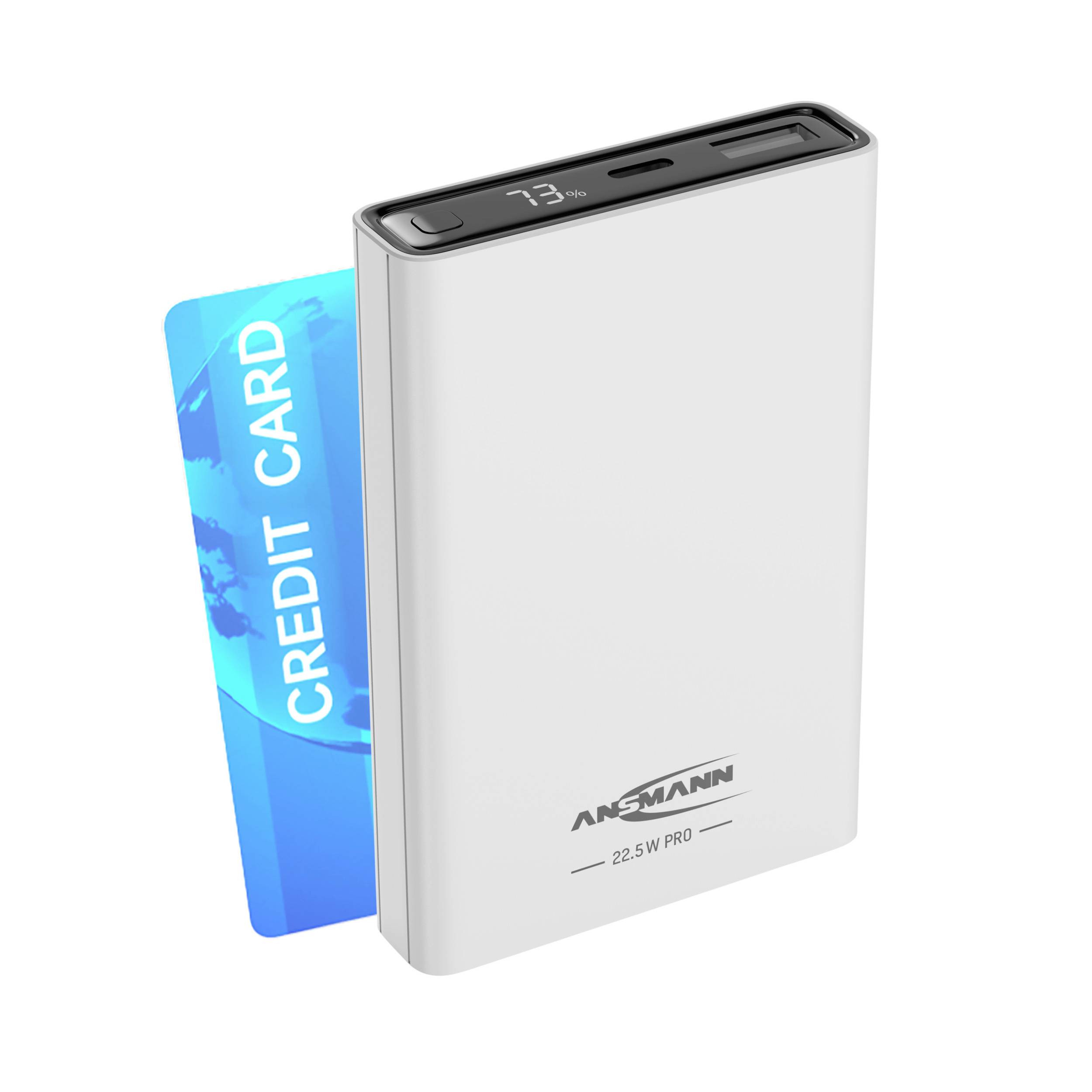 Bílá powerbanka s digitálním displejem a USB porty, vedle modré kreditní karty; ukazuje kompaktní velikost a přenositelnost.
