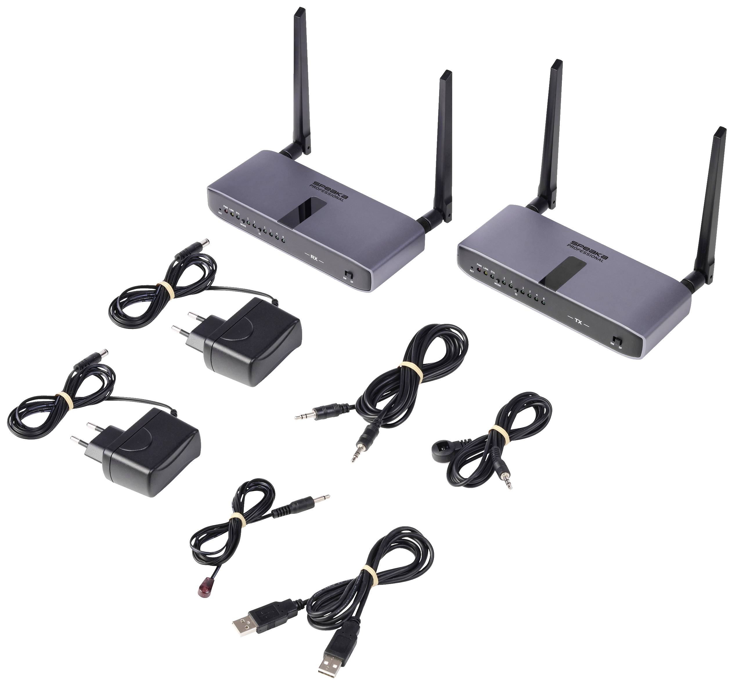 Dva šedé bezdrátové audio vysílače s anténami, tři napájecí zdroje a různé kabely, včetně USB a audio kabelů, na bílém pozadí.