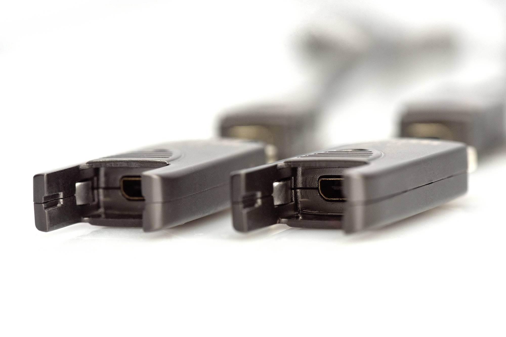 Několik černých plochých kabelů s konektory USB-C, které leží v řadě na bílém povrchu, s ostrou fokusací na konektory.