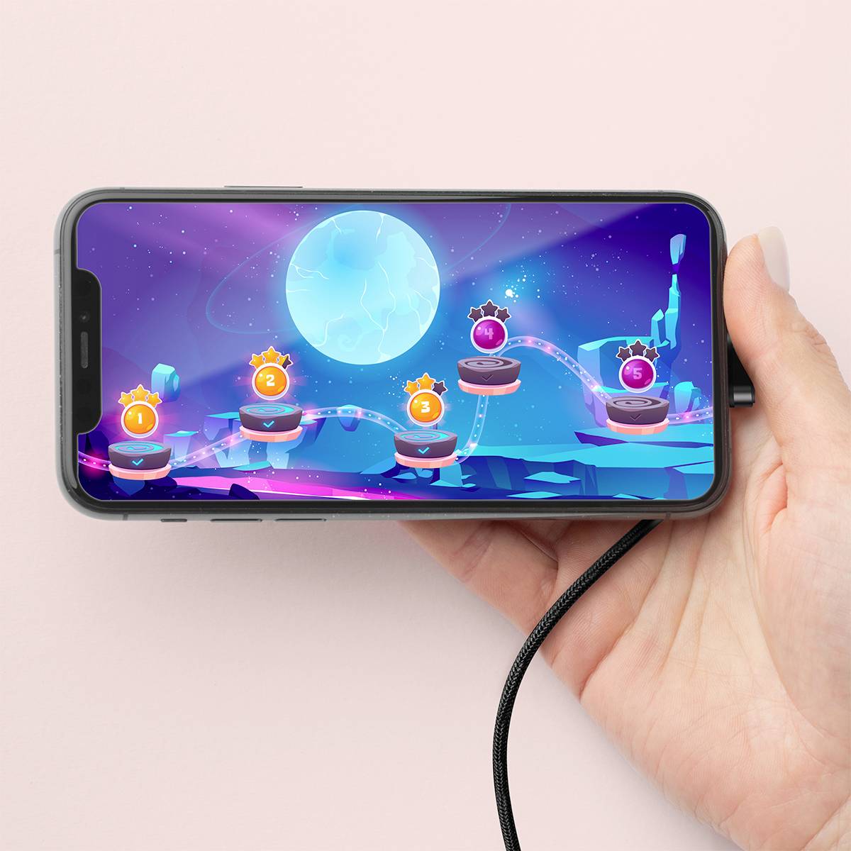 Ruka drží smartphone s videohrou na obrazovce, která zobrazuje level s osvětlenými kuličkami a modré, hvězdné vesmírné pozadí.