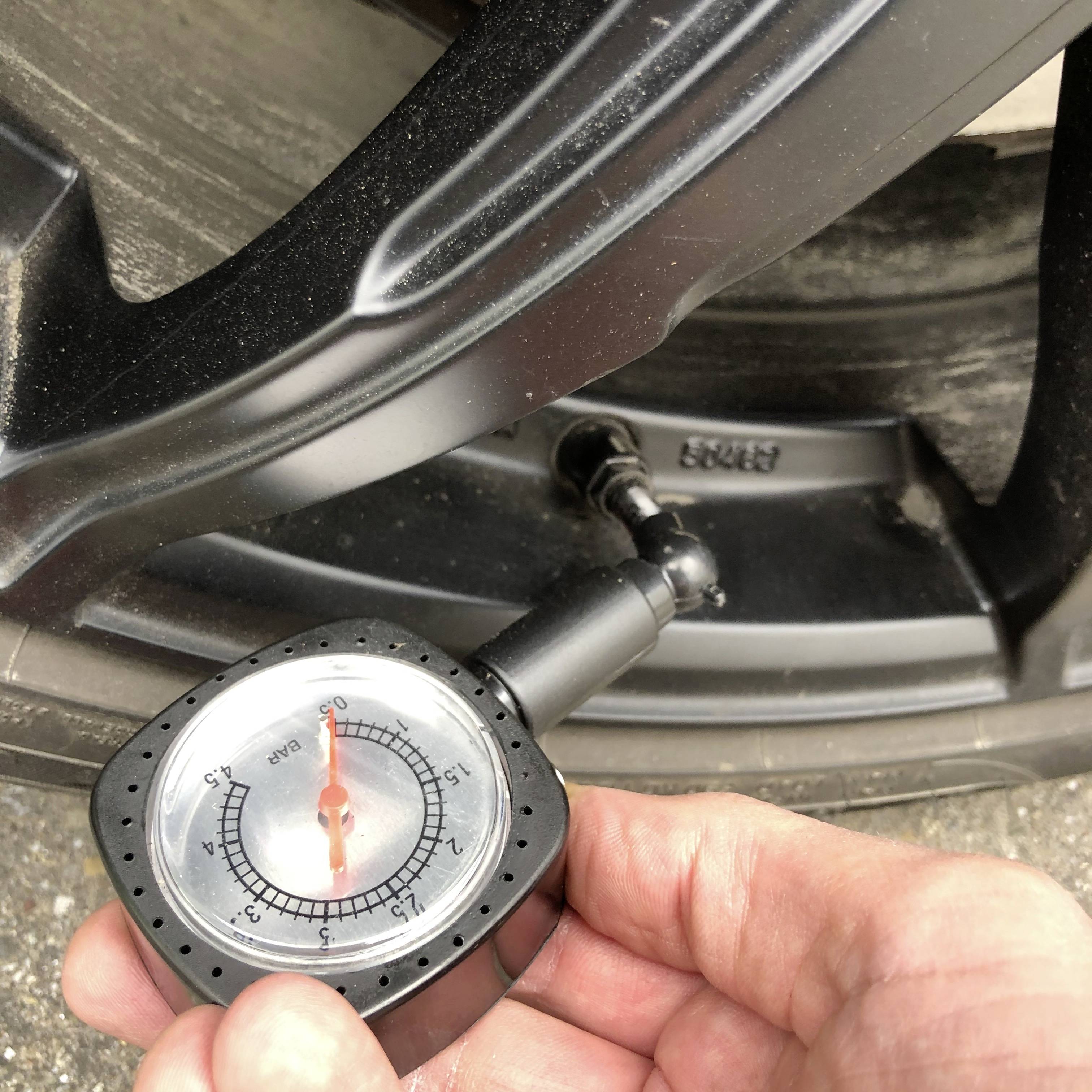 Manometr ukazuje tlak v pneumatice 2,5 baru, je držen v ruce a nasazen na ventilku automobilové pneumatiky.