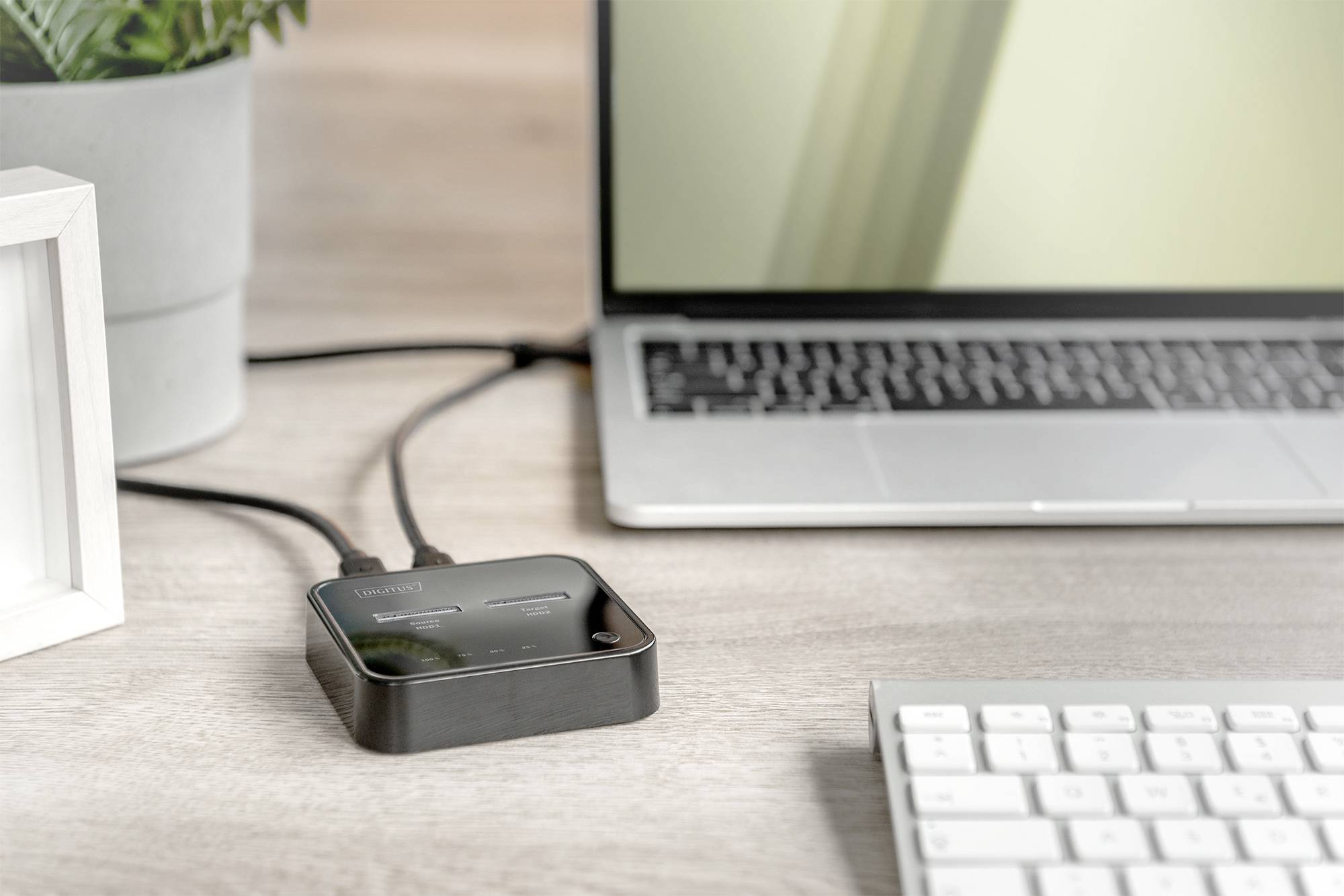 Laptop je připojen přes USB kabel k malému černému rozbočovači, který stojí na stole vedle klávesnice.