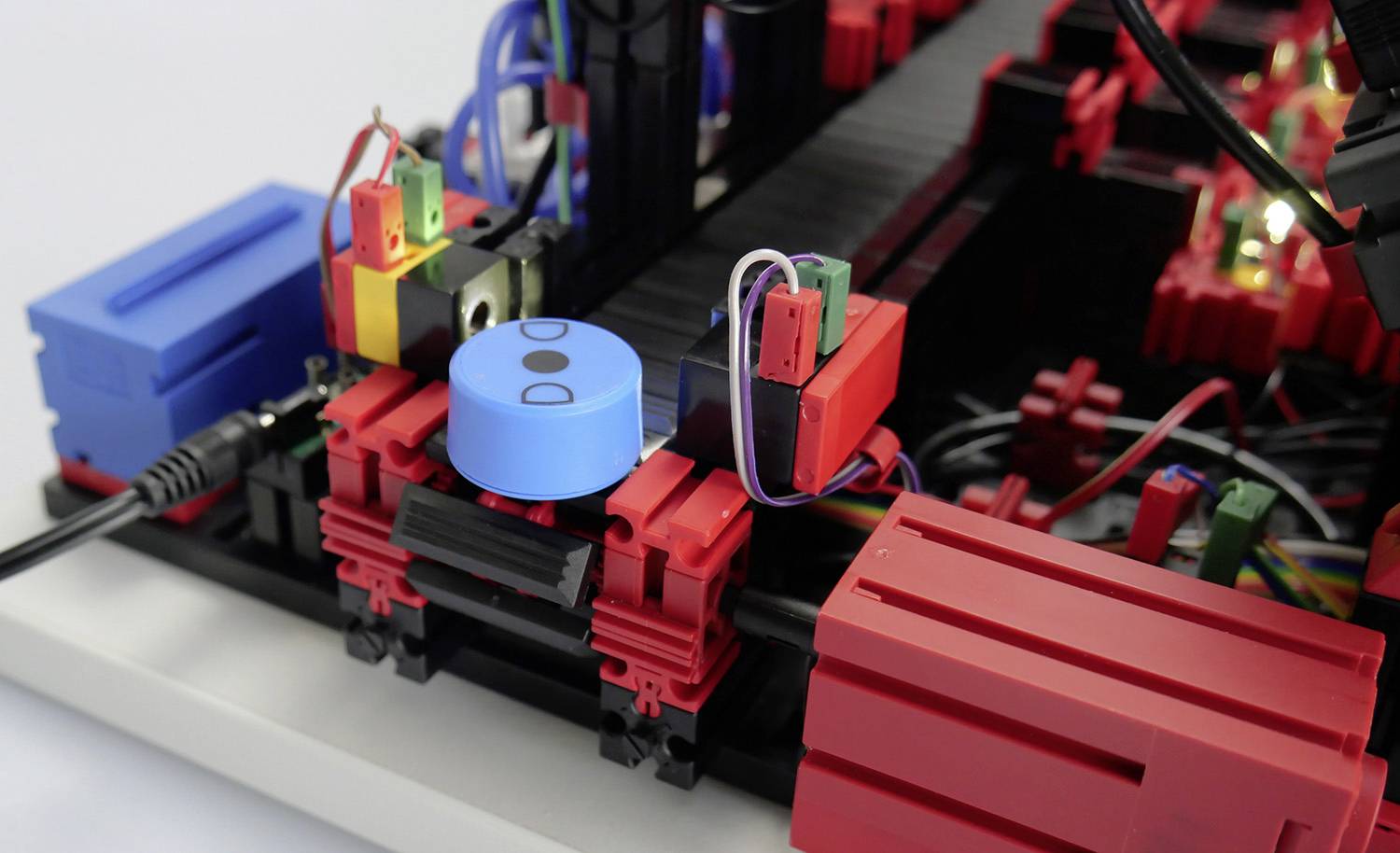 Detailní záběr elektronického zařízení s červenými a modrými komponenty, zapojený na desce. Komponenty vypadají modulární a propojitelné.