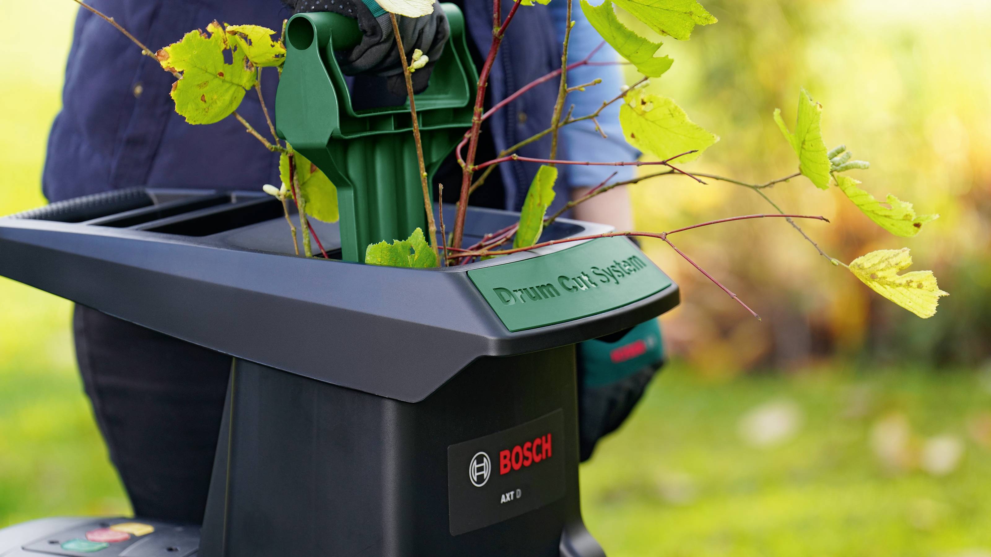 Osoba používá elektrický zahradní drtič od Bosche k rozdrcení větví a listí.