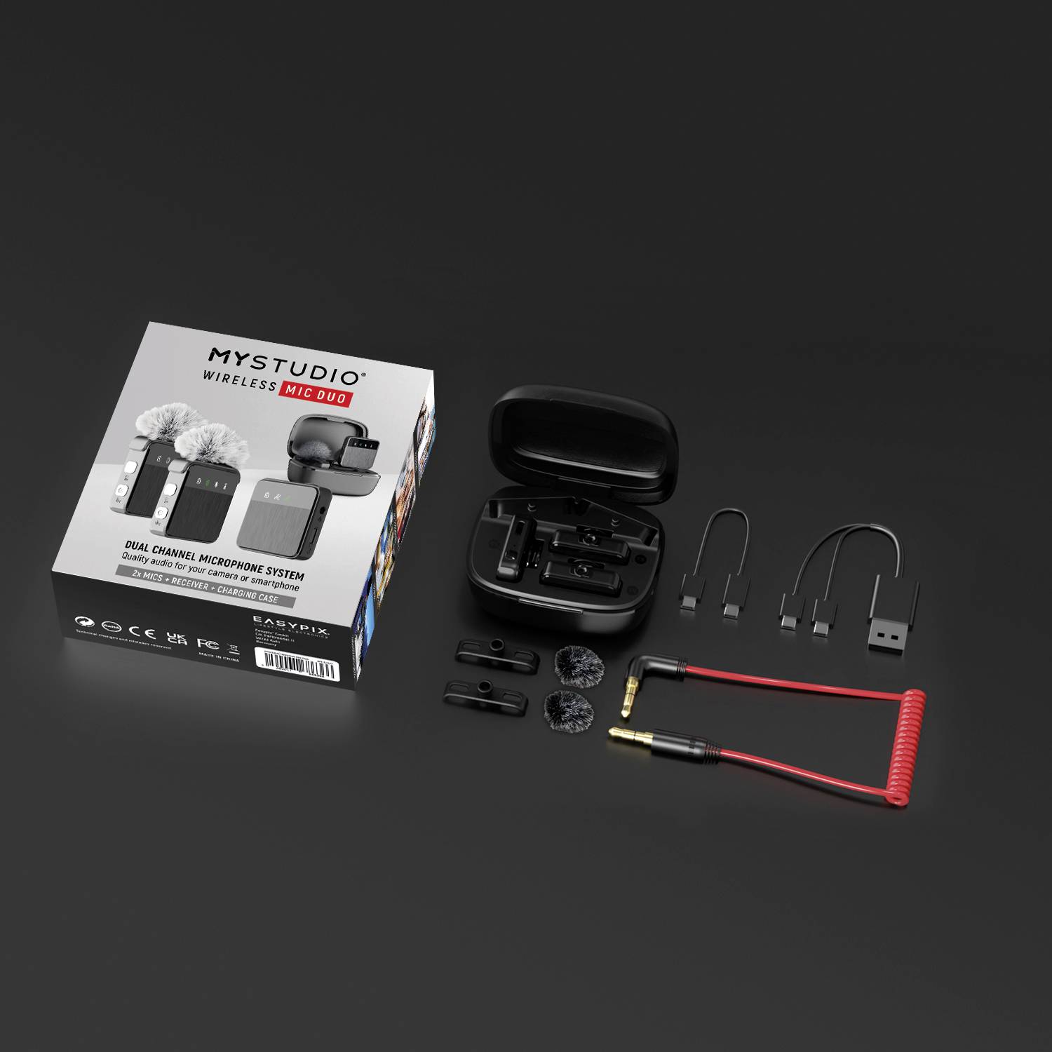 Pohled shora na MyStudio Wireless Mic Duo: mikrofony, nabíjecí pouzdro, kabel a příslušenství na černém povrchu. Balení vlevo.