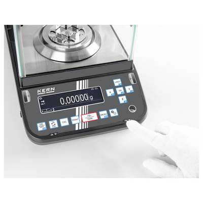 Elektronická váha zobrazuje hmotnost '0,00000 g'. Ruka v bílé rukavici se dotýká tlačítka 'TARE' vedle displeje.