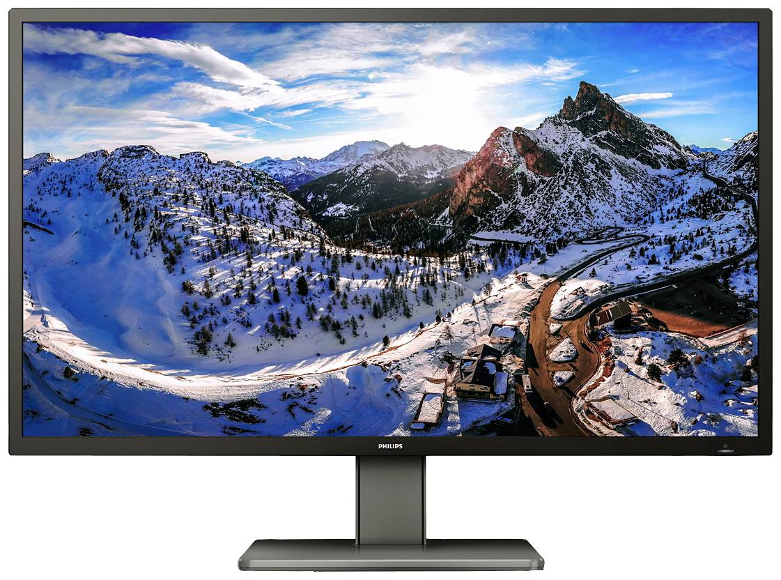 Velký monitor zobrazuje sněžnou krajinu v horách při západu slunce, s cestami a sporadicky rozmístěnými domy v popředí.