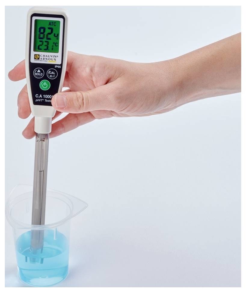 Jedna ruka drží digitální pH metr, který je ponořen do sklenice s modrou kapalinou. Displej zobrazuje pH 8,24 a teplotu 23,7°C.