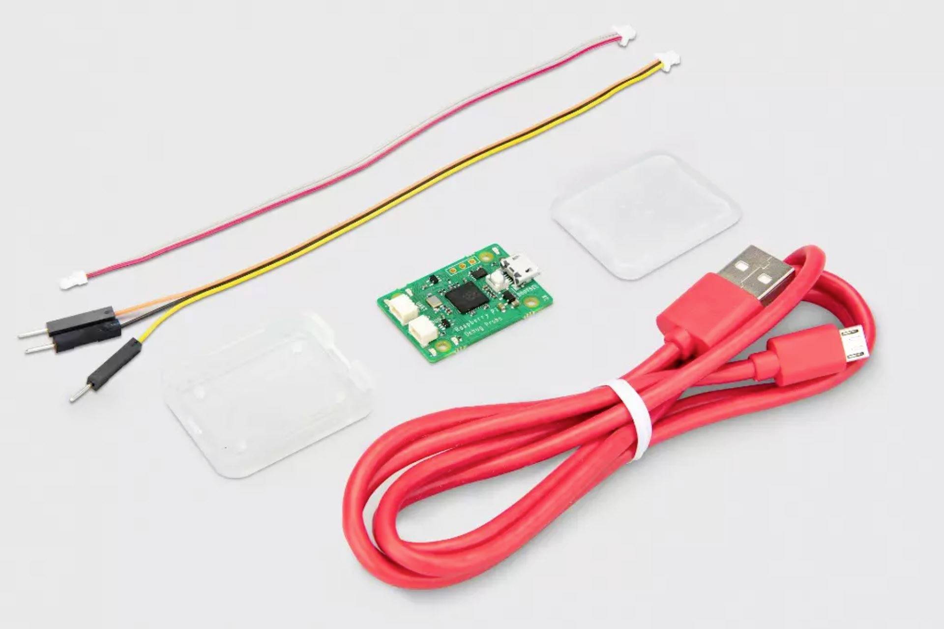 USB datový a nabíjecí kabel, malá zelená deska plošných spojů a dva svazky tenkých kabelů jsou uspořádány na světlém povrchu.