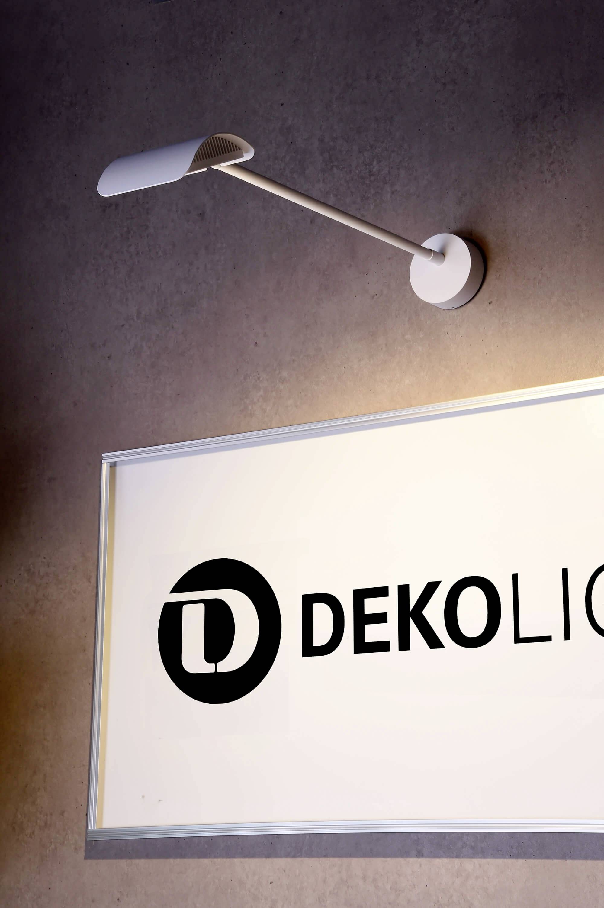Moderní nástěnné svítidlo osvětluje ceduli s nápisem 'DEKOLICHT' v minimalistickém, současném designu.
