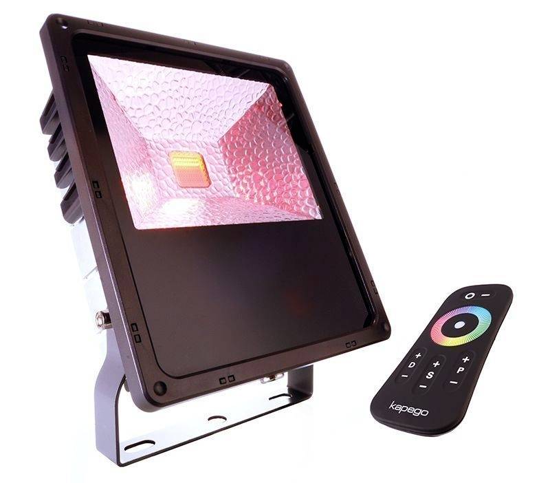 Černý LED reflektor s růžově svítícím vnitřním reflektorem, vedle černého dálkového ovladače s barevným kruhem a tlačítky.