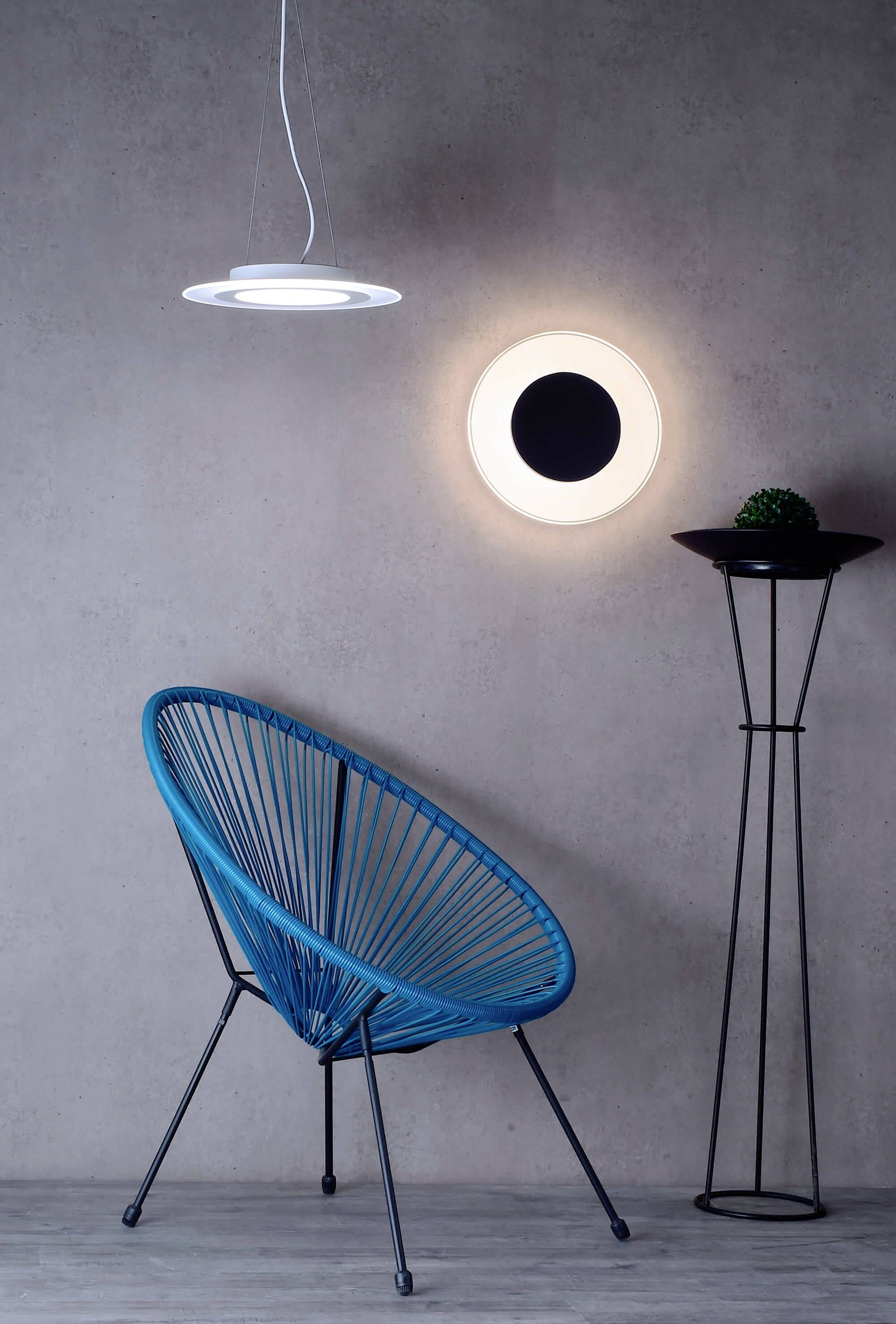 Modrá židle stojí vedle moderní stojací lampy a kulaté nástěnné lampy na šedé stěně. Elegantní, minimalistický design.