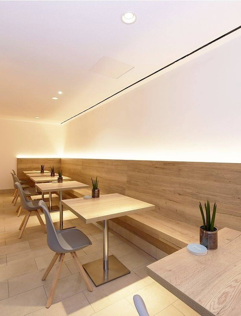 Moderní jídelna se dřevěnými stoly a šedými židlemi. Malé rostliny slouží jako dekorace. Teplé osvětlení vytváří útulnou atmosféru.