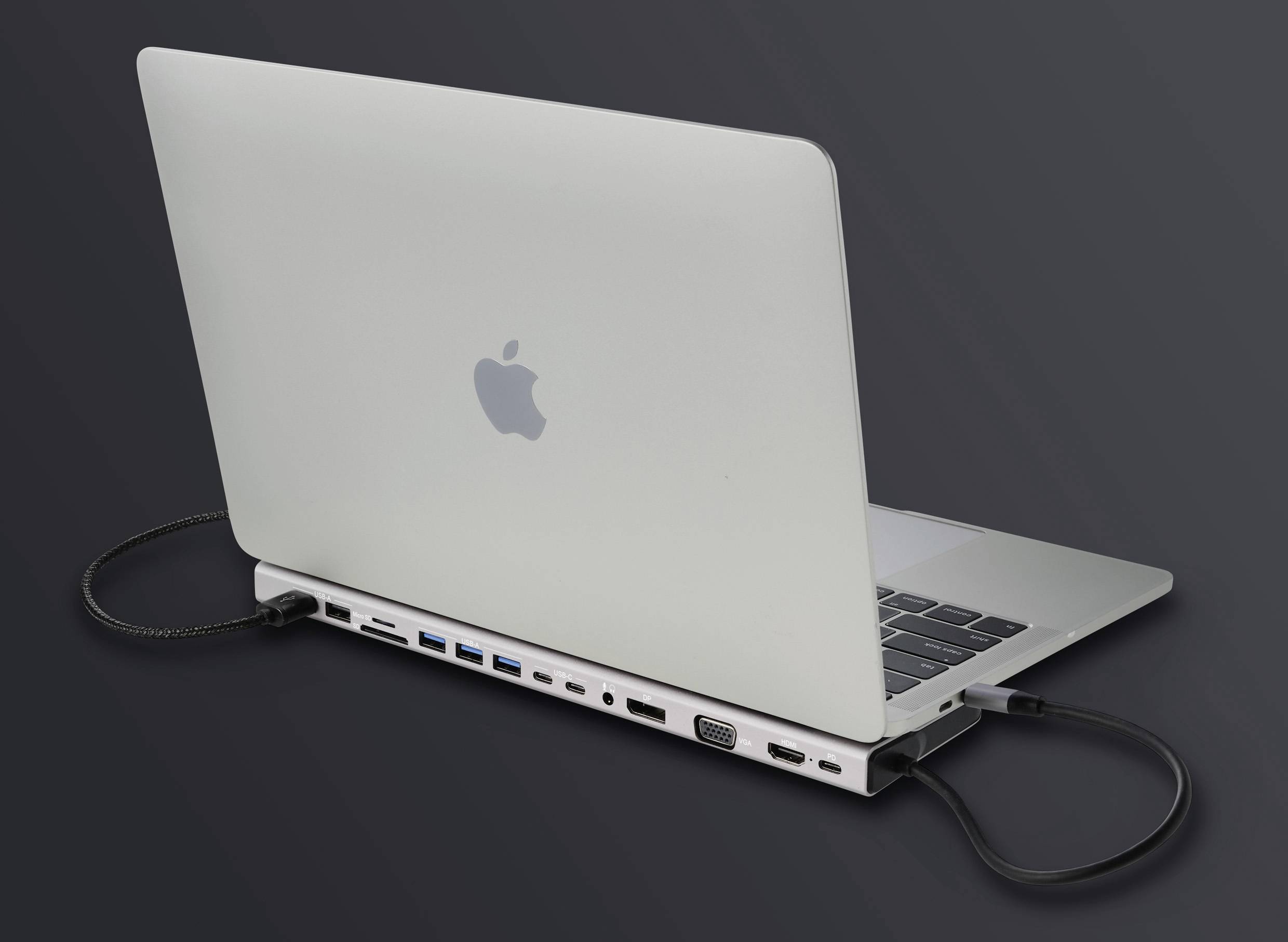 Notebook je připojeno k dokovací stanici, která nabízí několik portů, včetně USB, HDMI a VGA, na tmavém pozadí.