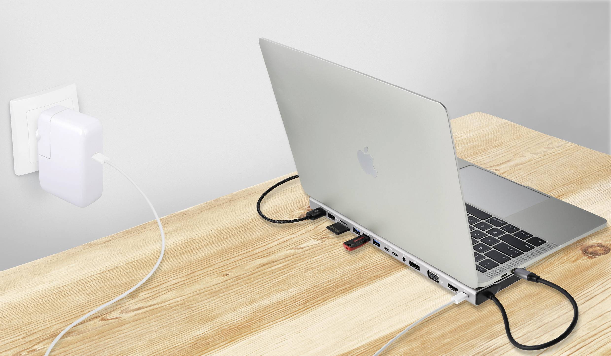 Notebook položené na stole, propojené několika kabely a nabíjecím adaptérem zapojeným do elektrické zásuvky, zobrazuje pracovní stanici.