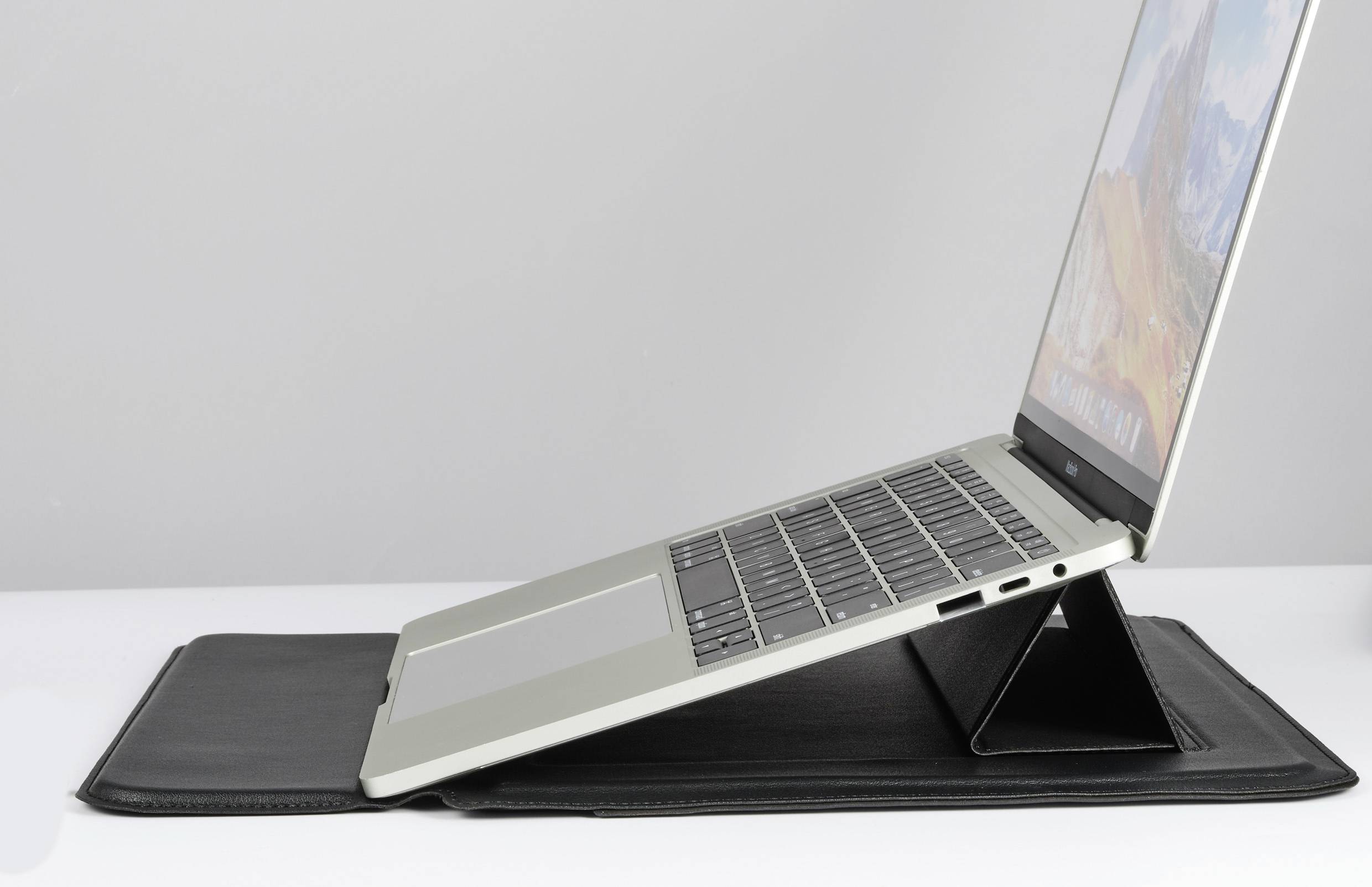 Rozevřený laptop stojí na černém stojanu na stole. Na obrazovce je barevný krajinný snímek.