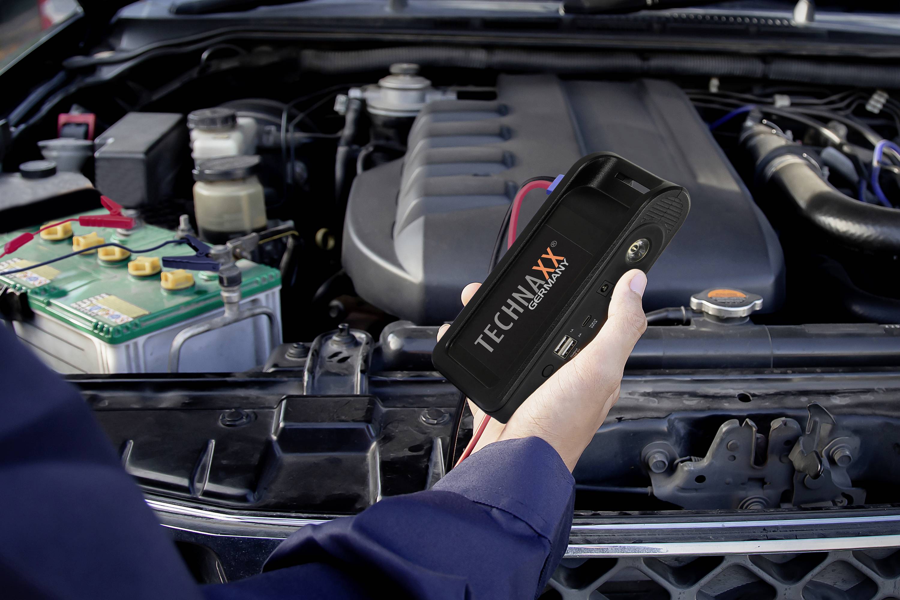Osoba drží startovací kabel poblíž autobaterie v motorovém prostoru vozidla.