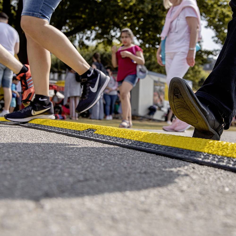 Detailní záběr lidí procházejících se po chodníku za slunečného počasí. V pozadí jsou další chodci.