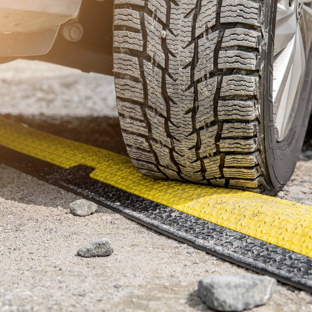 Kolo automobilu přejíždí žlutý práh na asfaltované silnici.