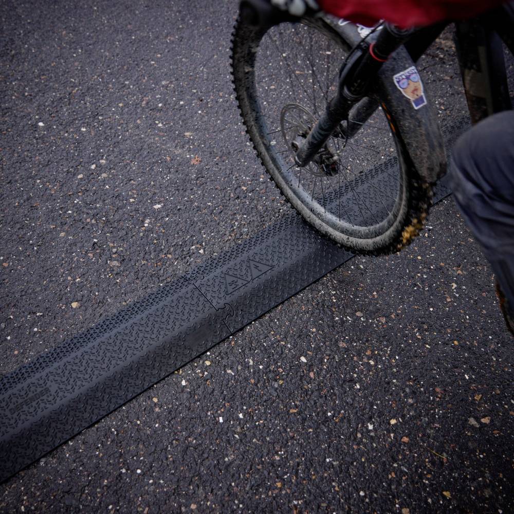Cyklista projíždí přes zpomalovací práh na silnici; zaměření je na pneumatiku a hranu prahu v okamžiku nárazu.