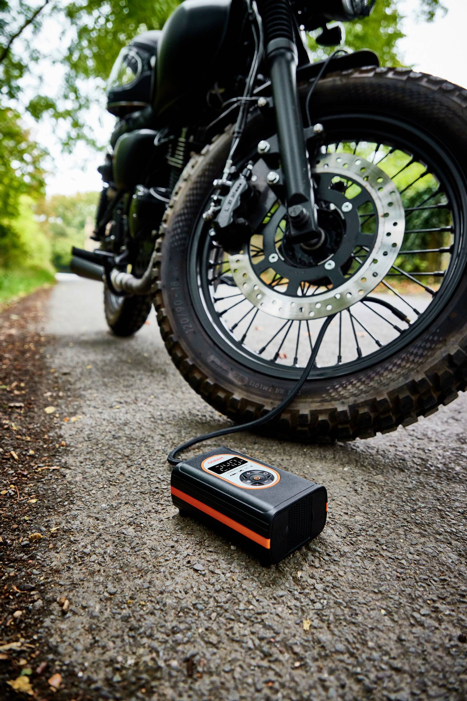 Motocykl na okraji silnice, pneumatika se nafukuje přenosným kompresorem. V pozadí příroda.