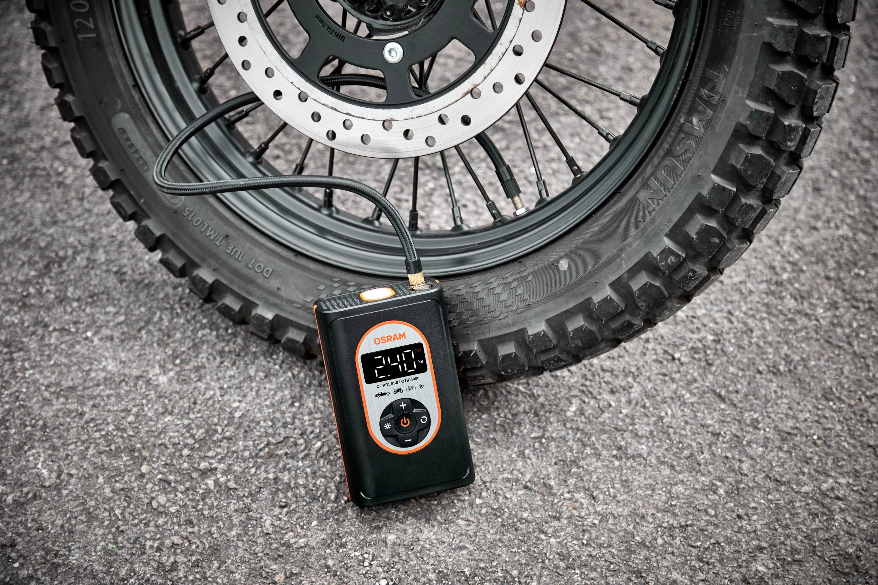 Přenosný kompresor nafukuje pneumatiku motocyklu. Digitální displej ukazuje tlak 2,1 baru.