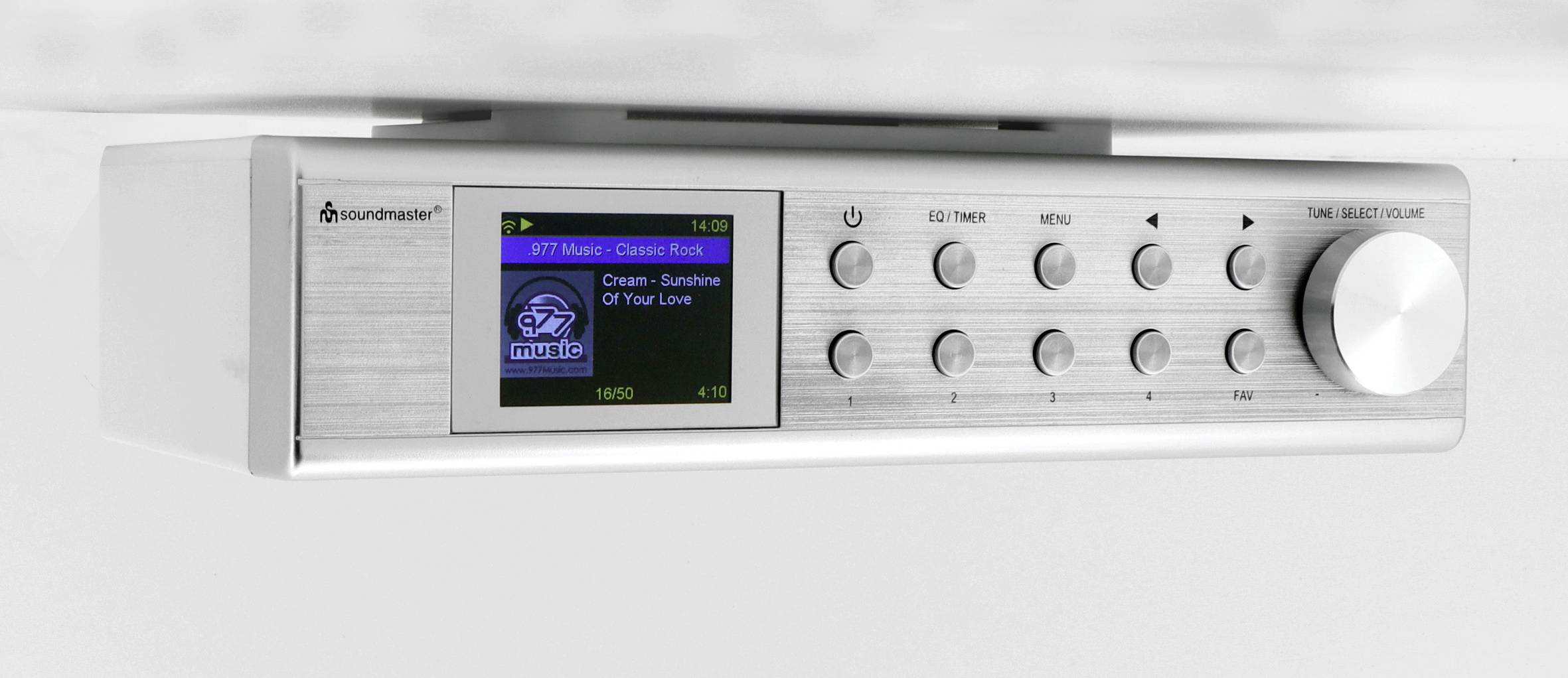 Stříbrné rádio s digitálním displejem zobrazuje '87.7 MHz, Classic Rock'. Ovládací tlačítka a regulátor hlasitosti jsou umístěny vpravo.