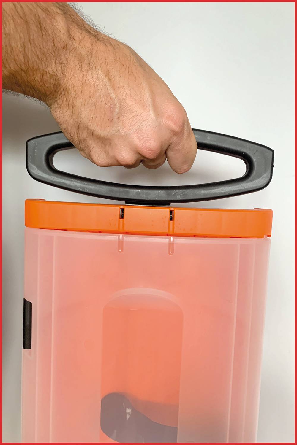 Ruka drží rukověť oranžového kontejneru, zobrazeno na bílém pozadí.
