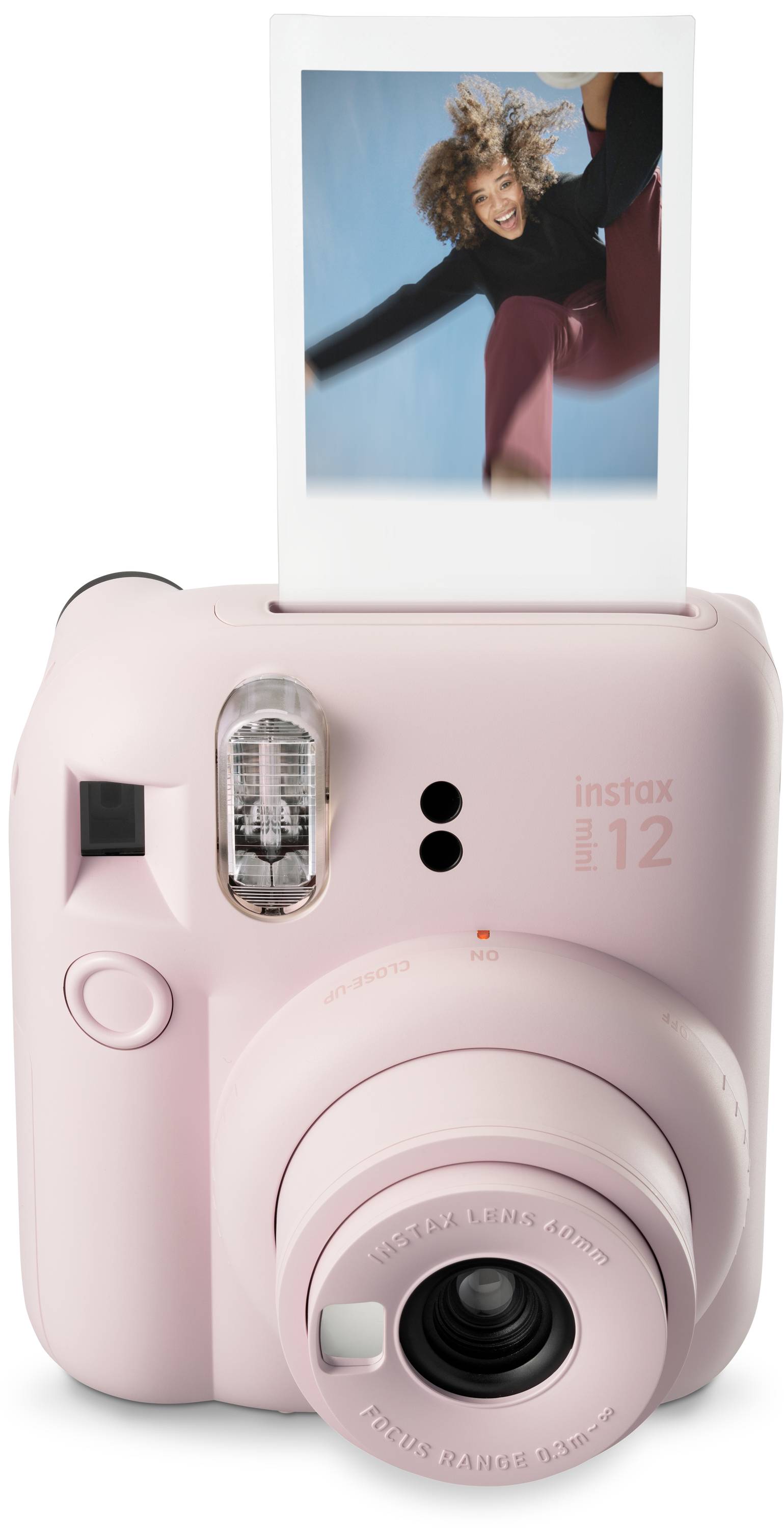 Růžový instantní fotoaparát tiskne fotografii vesele skákající osoby.