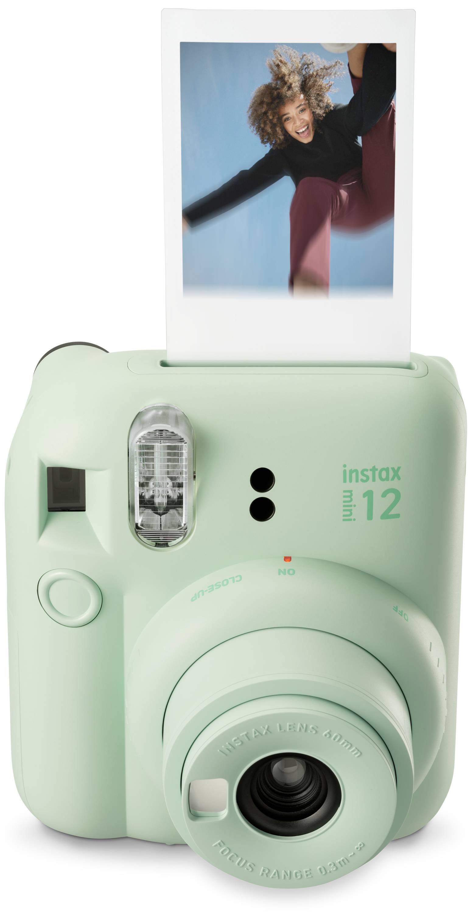Mátově zelený instantní fotoaparát s již vytištěnou fotografií, která zachycuje radostnou osobu při skoku.