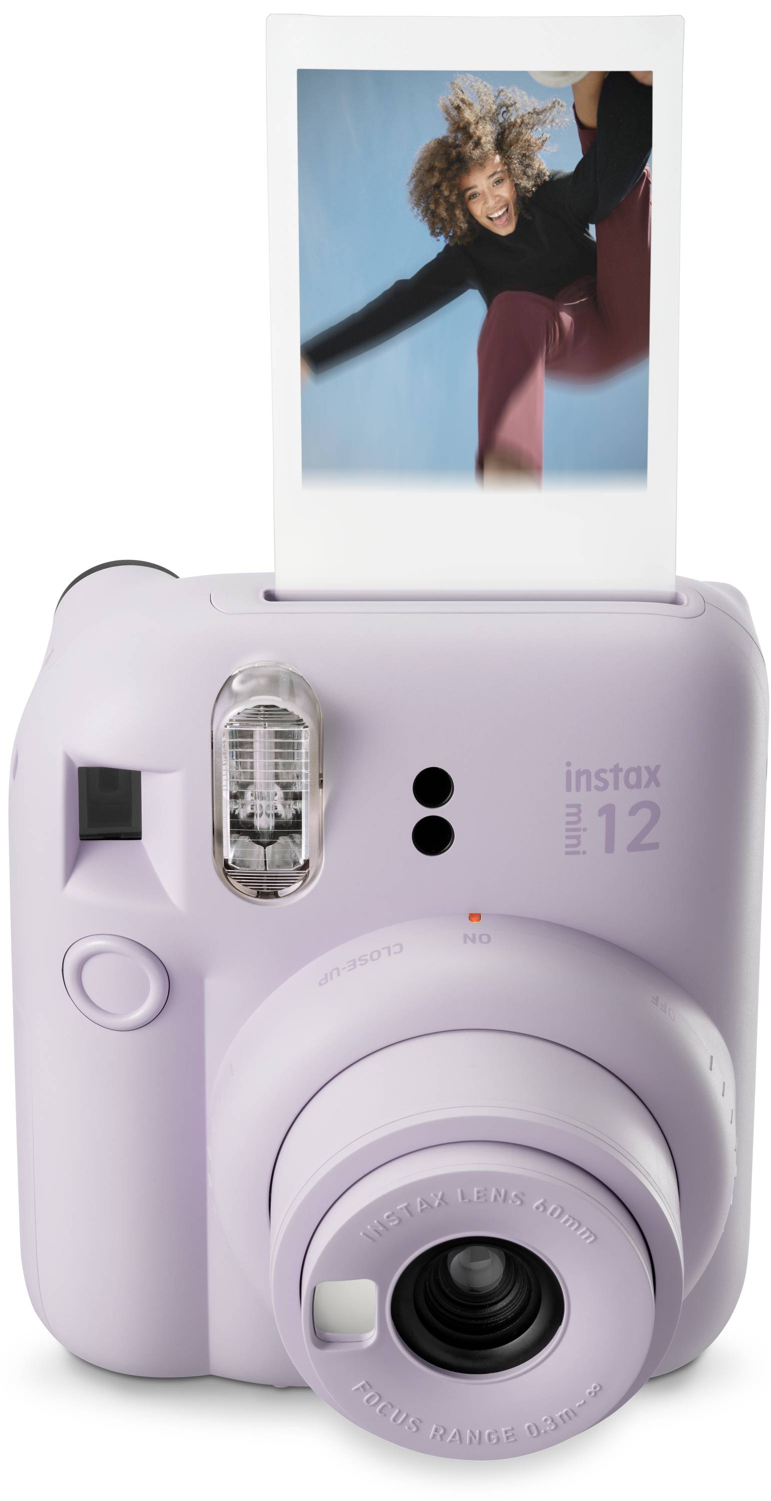 Fialový instantní fotoaparát s vyvolanou fotografií, na které je osoba vesele skákající.