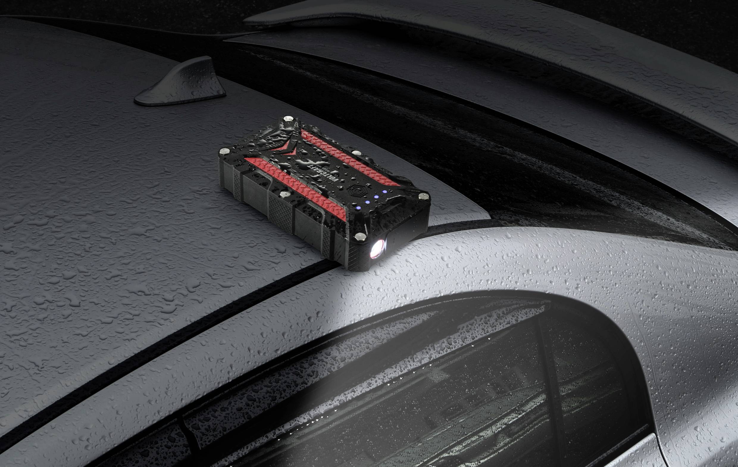 Černá a červená přenosná powerbanka leží na mokré střeše automobilu. Zařízení svítí a vytváří jasný světelný paprsek.