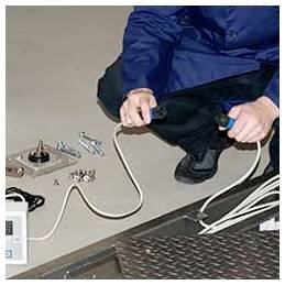 Osoba dřepí u otevření v kovové podlaze a drží elektrický kabel a pracuje s nástroji a hardwarem na zemi.