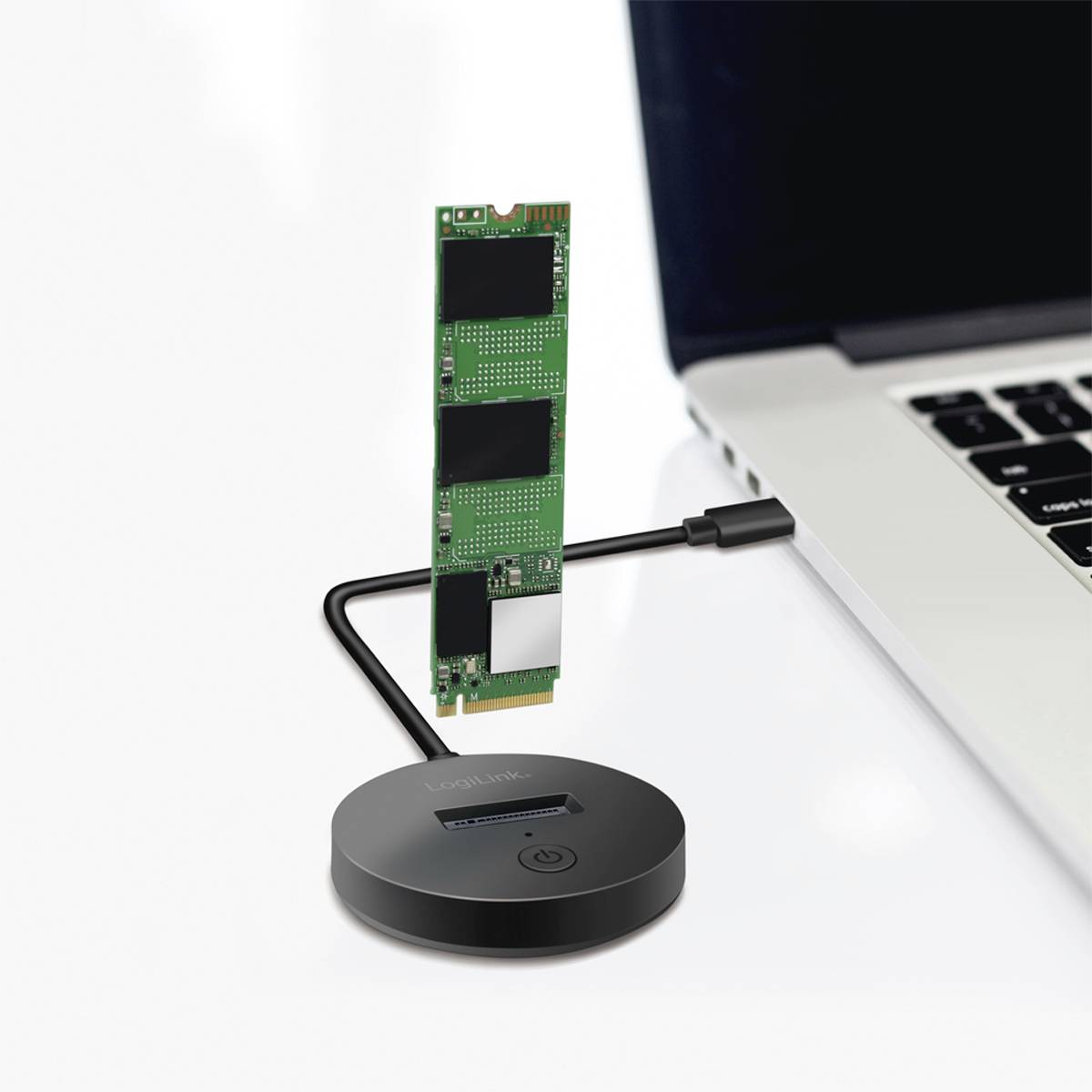 SSD stojí vzpřímeně na černém kulatém USB rozbočovači, který je připojen k notebooku.