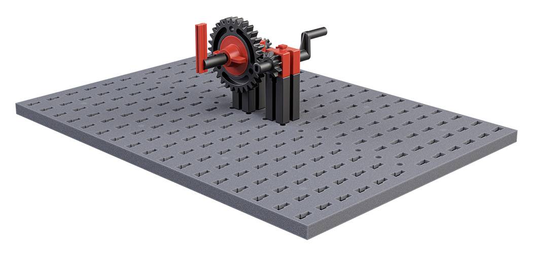 Mechanismus ozubeného kola s klikou, namontovaný na šedé, tečkované základní desce.