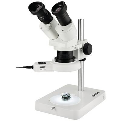 Bílý stereomikroskop se dvěma okuláry stojí na stole. Pod ním leží malý elektronický obvod na osvětlené základně.