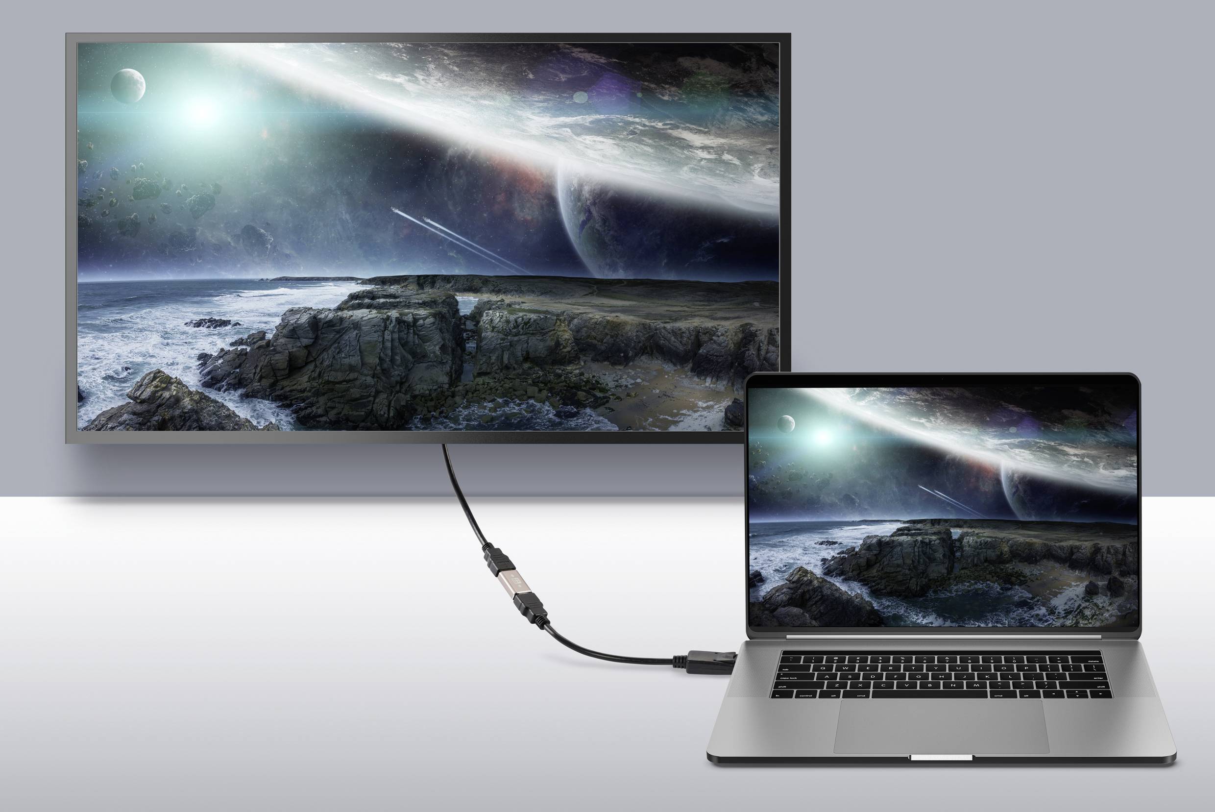 Notebook je připojeno kabelem k monitoru. Oba displeje zobrazují digitální vesmírnou krajinu s planetami a hvězdami.