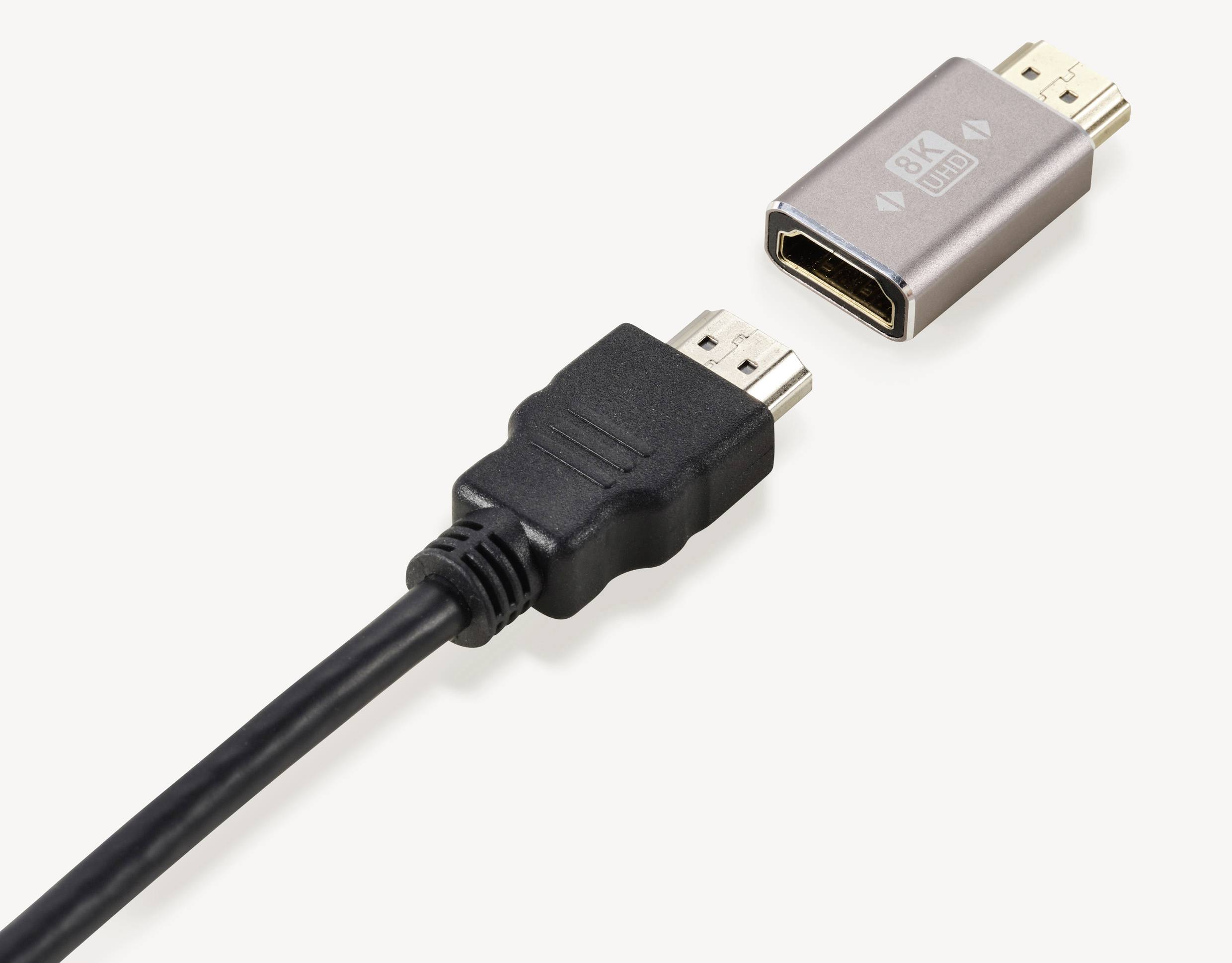 Dva kabely: vlevo černý HDMI kabel, vpravo stříbrný HDMI adaptér s nápisem '8K'.