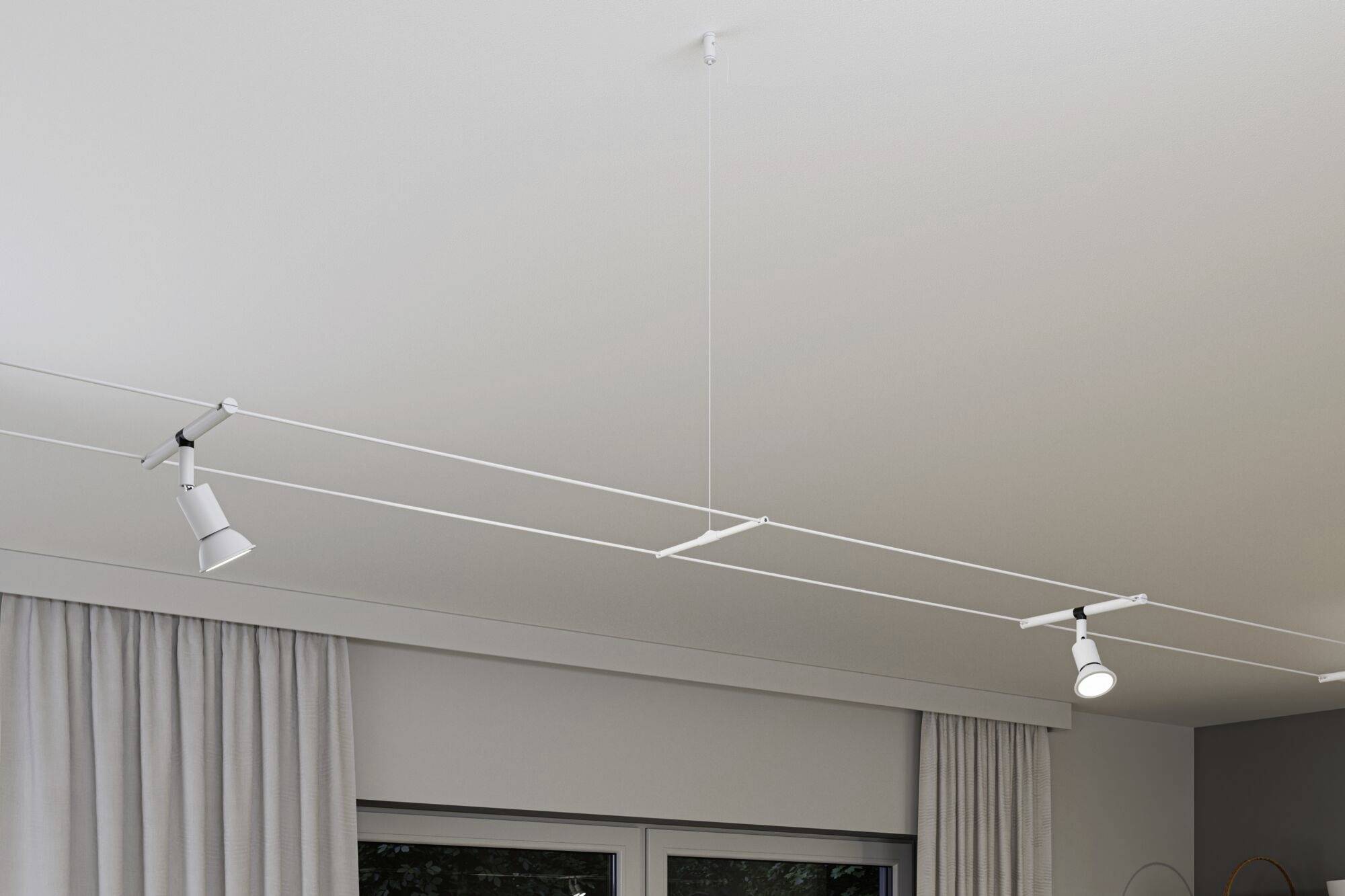 Bílé, minimalistické stropní svítidlo se třemi nastavitelnými reflektory, instalované v moderním prostoru s světle šedými závěsy.