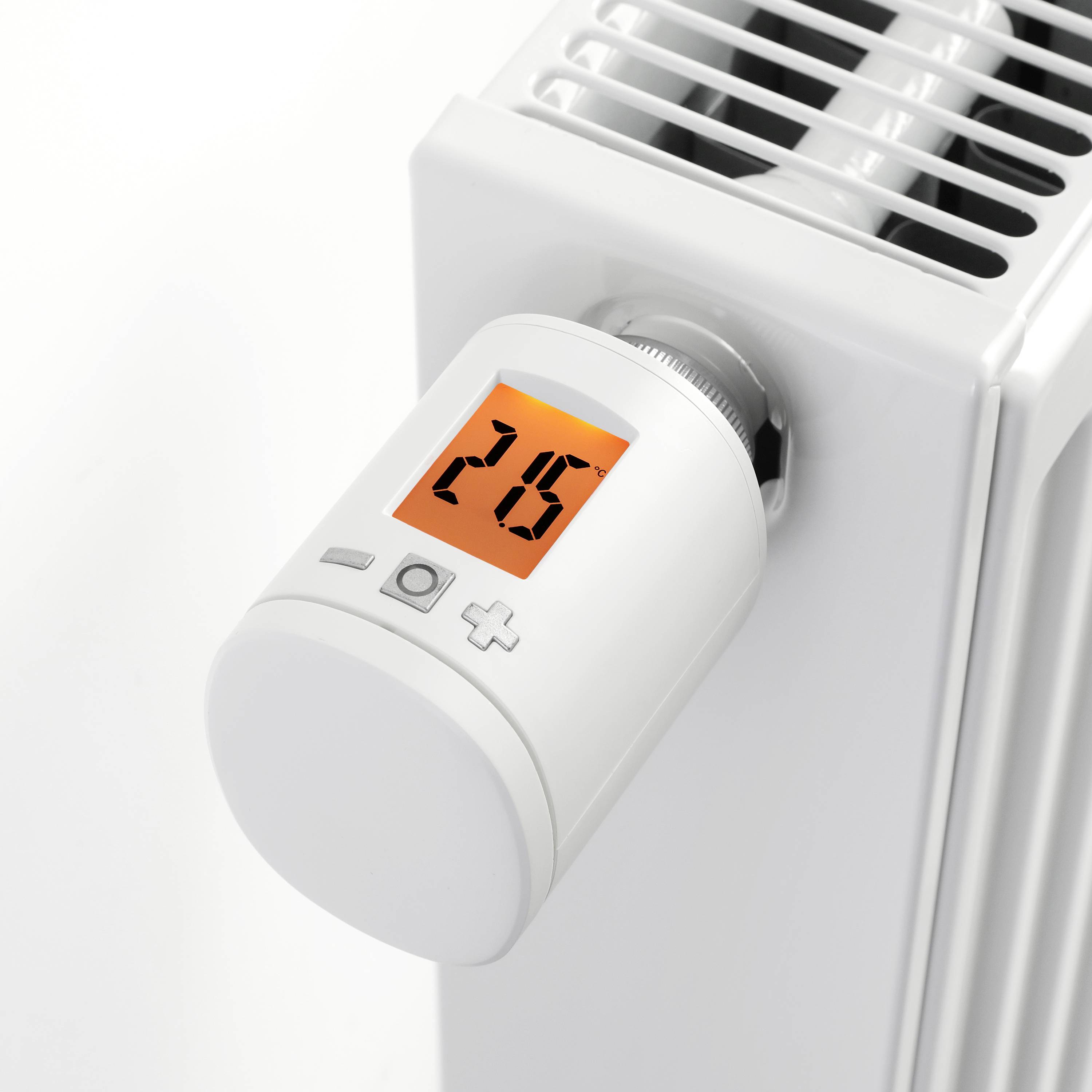 Moderní termostatická hlavice ukazuje 26 stupňů Celsia na digitálním displeji, umístěná na bílém radiátoru.
