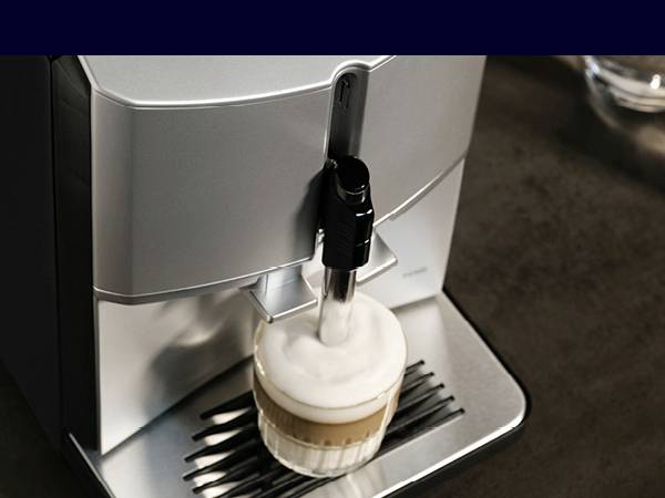 Kávový přístroj připravuje cappuccino. Káva je nalévána do šálku, který stojí na stříbrné odkapávací mřížce.