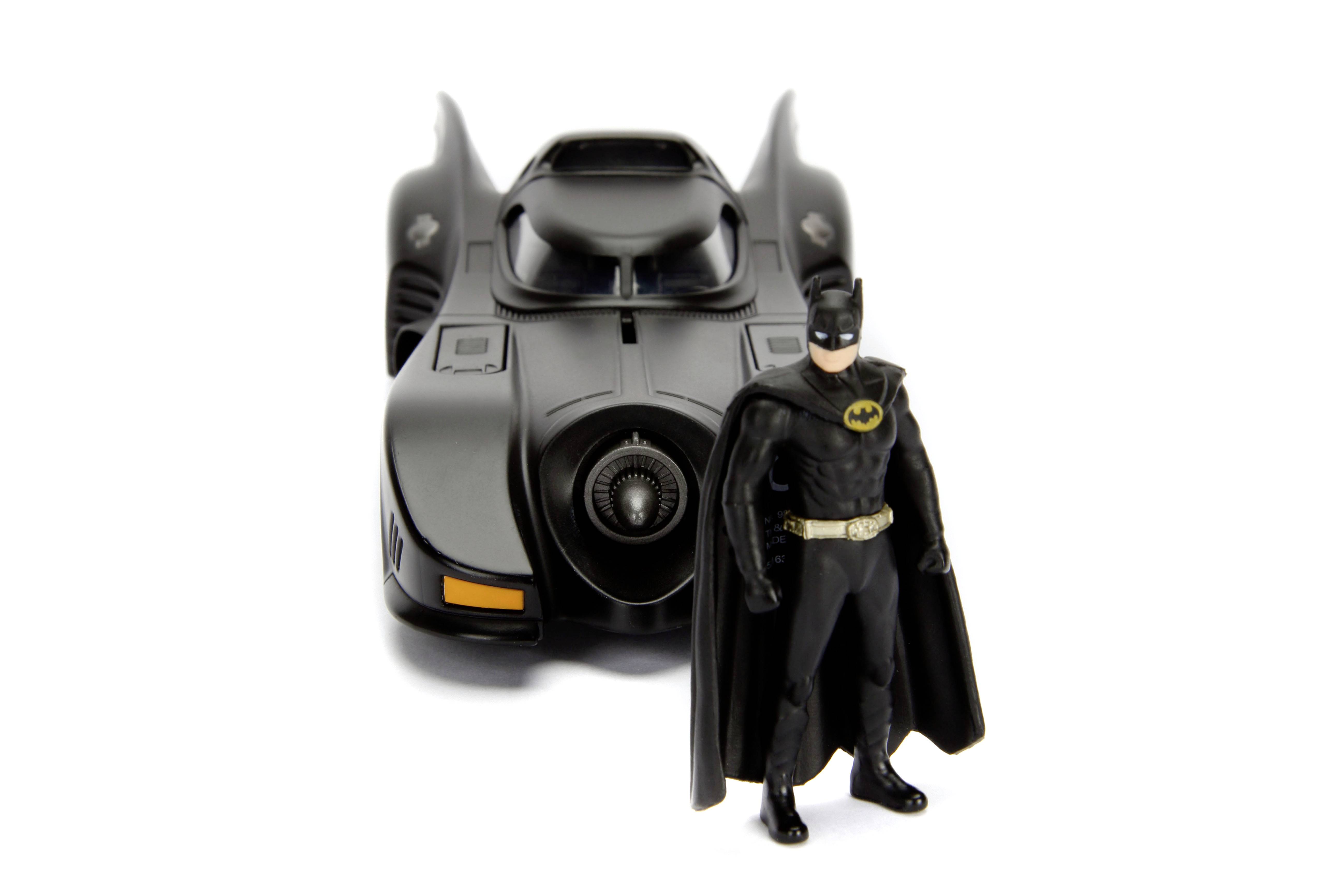 Akční figurka Batmana stojí před modelem Batmobilu na bílém pozadí.