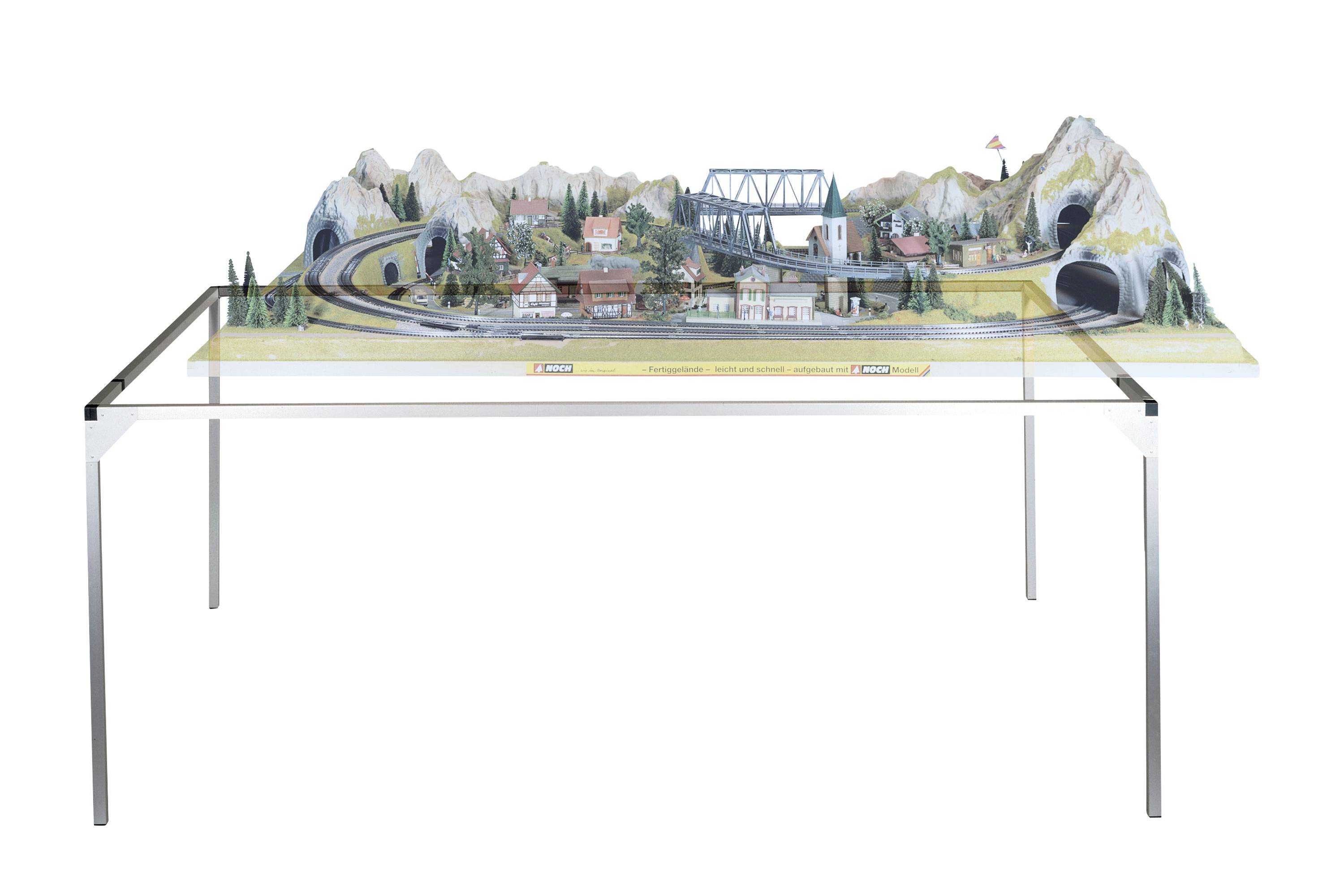 Skleněný stůl s krajinou modelové železnice. Jsou zde vidět hory, tunel, most a malá vesnice.