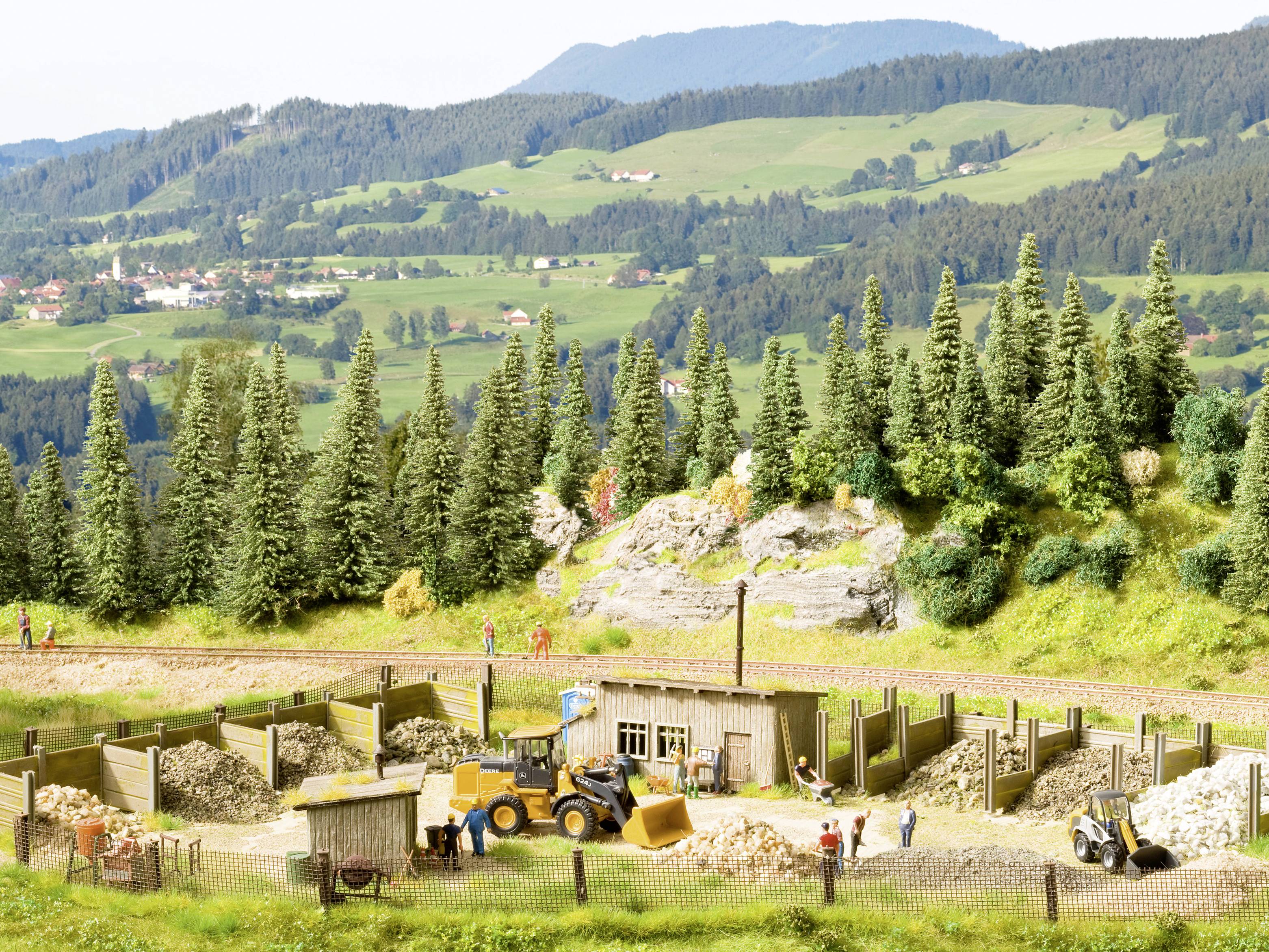 Krajinné diorama ukazuje oblast staveniště s bagrem a dělníky, obklopenými lesy a horami v pozadí.
