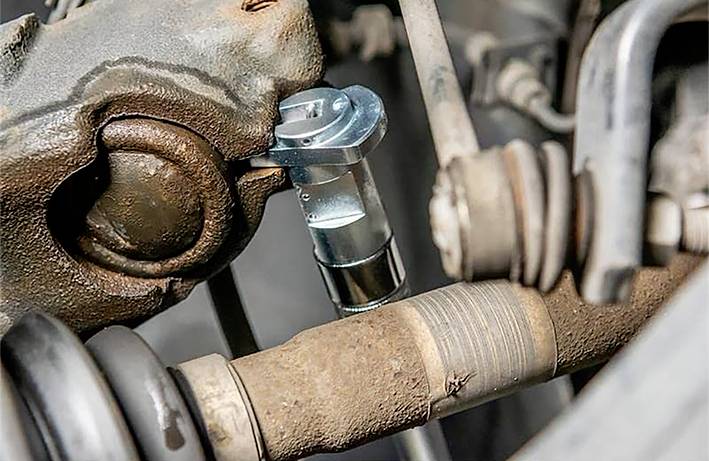 Detail motorových součástí automobilu. Je vidět kardanový hřídel a další mechanické komponenty v zrezavělém stavu.