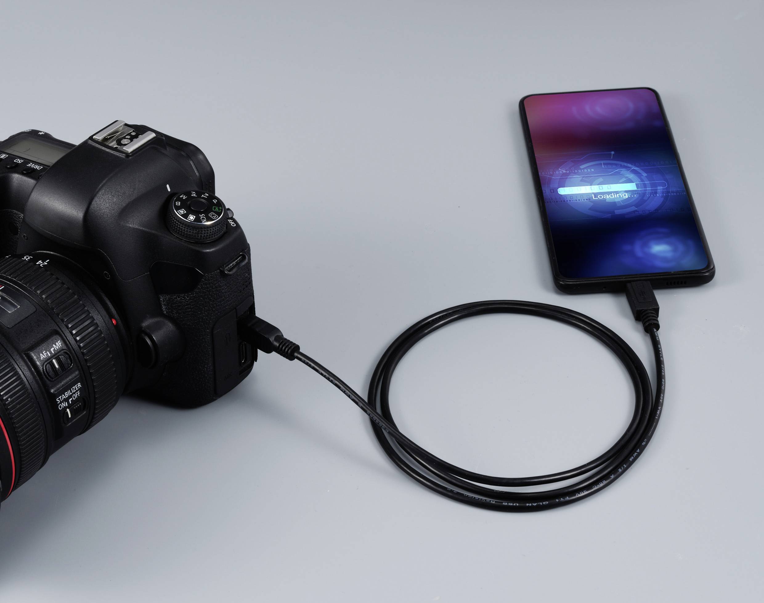 Fotoaparát připojený ke smartphonu pomocí USB kabelu. Na displeji smartphonu je zobrazeno 'Probíhá nabíjení'.