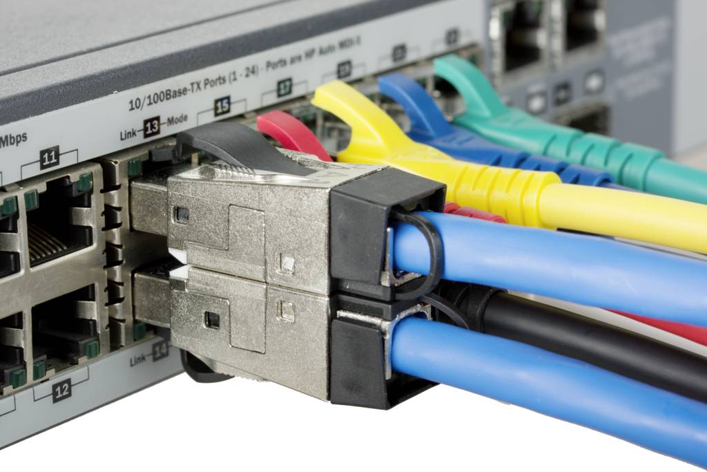 Detailní záběr síťového switche s několika zapojenými ethernetovými kabely v různých barvách, znázorňující síťové připojení.