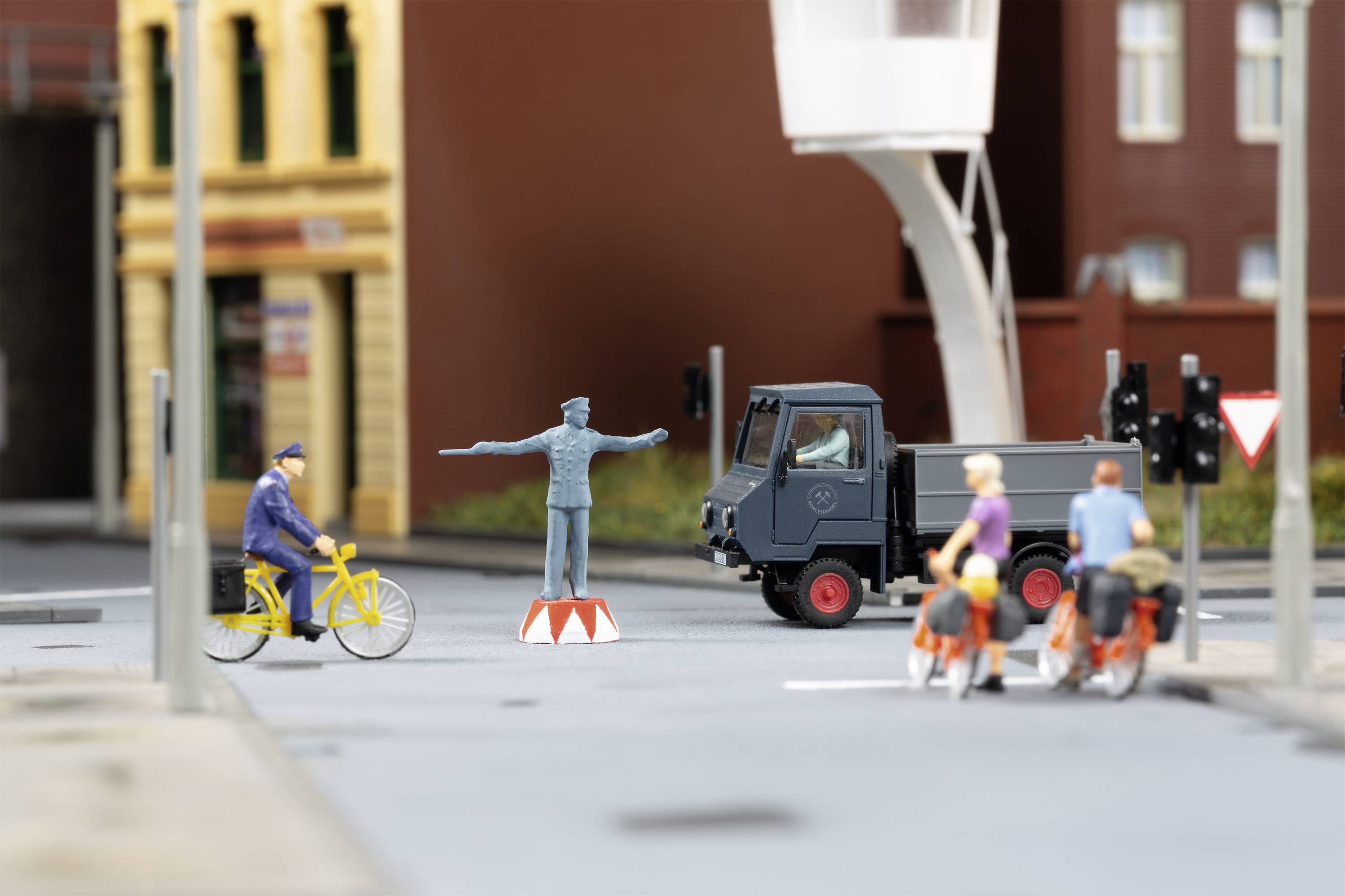 Miniaturní scéna zobrazuje město s nákladním vozem, policistou na podstavci, cyklisty a chodci.