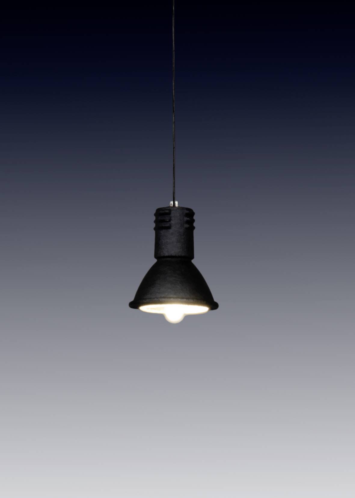 Visící žárovka vyzařuje teplé světlo v tmavé místnosti a vytváří jednoduchou a minimalistickou atmosféru.